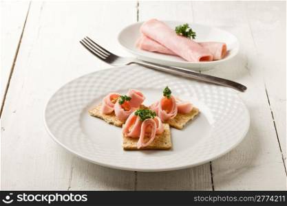photo of cracker appetizer with ham and parsley on white wooden table
