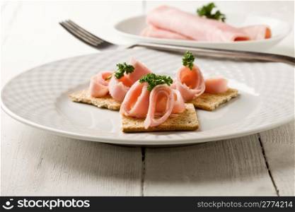 photo of cracker appetizer with ham and parsley on white wooden table