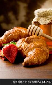 photo of croissants with honey and strawberries on wooden table