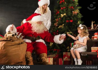Photo of cute girl and her mother and Santa Claus at home near Christmas tree