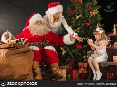 Photo of cute girl and her mother and Santa Claus at home near Christmas tree