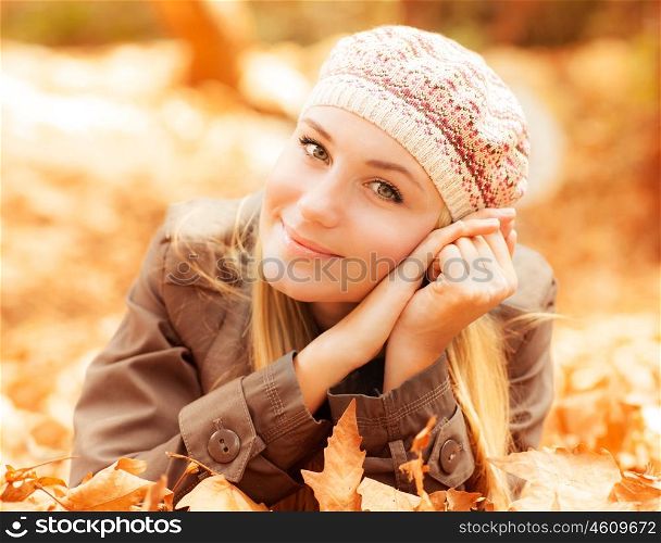 Photo of cute girl laying down on the ground covered dry autumnal foliage in beautiful park in sunny day, closeup portrait of pretty woman enjoying warm autumn sunlight, joy and fun concept