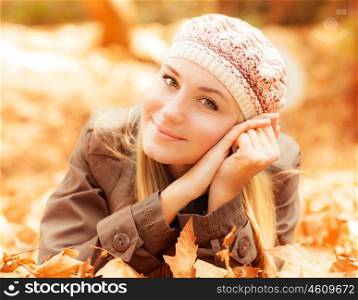 Photo of cute girl laying down on the ground covered dry autumnal foliage in beautiful park in sunny day, closeup portrait of pretty woman enjoying warm autumn sunlight, joy and fun concept
