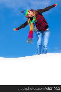 Photo of cute happy female enjoying winter holidays, nice teenager girl having fun outdoor at wintertime, pretty woman wearing colorful hat and scarf standing with hands up on snowy ground in the park