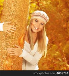 Photo of cute happy girl in autumnal park, closeup portrait of sweet blonde woman wearing stylish beret, attractive female hugging tree trunk in beautiful golden autumn woods&#xA;&#xA;