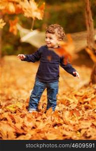 Photo of cute little boy enjoying autumnal nature, pretty infant playing in park, cheerful baby boy having fun outdoors, adorable kid in fall forest, happy child play with dry orange maple leaves&#xA;&#xA;
