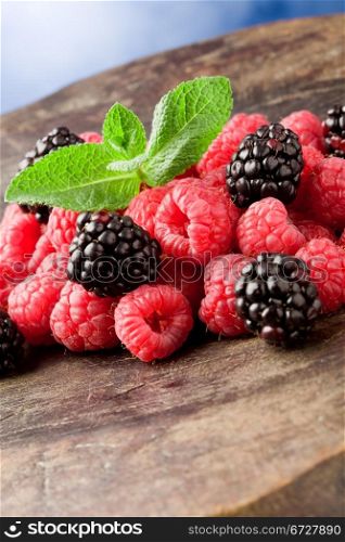 photo of delicious berries with meant leaves on wooden table