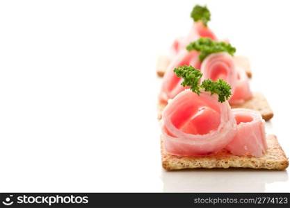 photo of delicious crackers with ham and parsley on white background