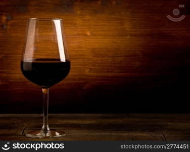 photo of delicious dark red wine goblet on wooden table illuminated by spot