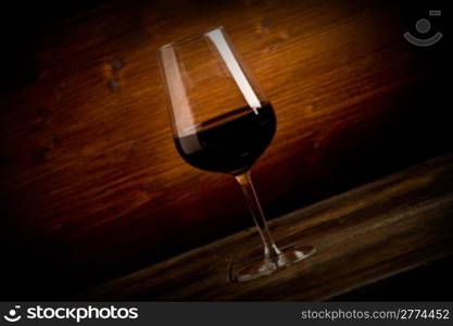 photo of delicious dark red wine goblet on wooden table illuminated by spot