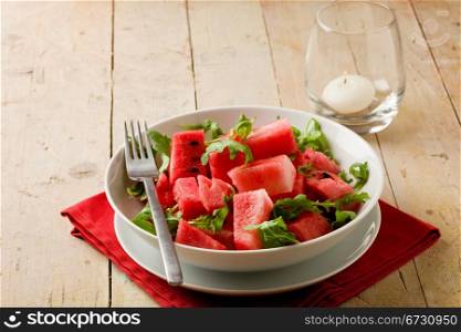 photo of delicious fresh watermelon and arugula salad on wooden table