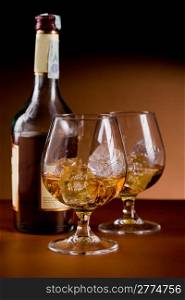photo of delicious glass of cognac whiskey with ice cubes on brown background