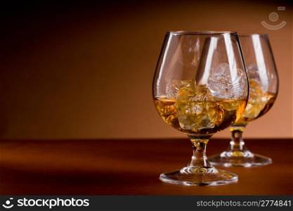 photo of delicious glass of cognac whiskey with ice cubes on brown background