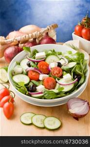 photo of delicious greek salad on wooden table in front of blue background with spot light