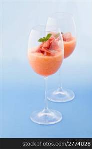 photo of delicious ham and melon cocktail appetizer on light blue background