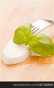 photo of delicious juicy mozzarella with basil leaf on wooden cutting board