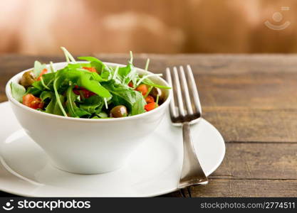 photo of delicious light salad with arugula and tomatoes in white bowl on wooden table