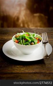photo of delicious light salad with arugula and tomatoes in white bowl on wooden table