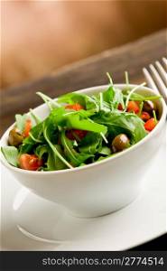 photo of delicious light salad with arugula and tomatoes in white bowl on wooden table