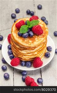 Photo of delicious pancakes with berries over wooden table