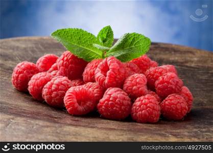 photo of delicious red raspberries with mint leaves on wooden table