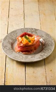 photo of delicious sliced bacon with melon inside on wooden table