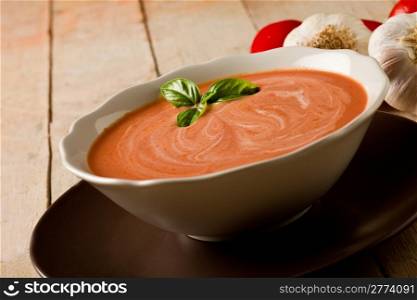 photo of delicious tomato cream soup on wooden table with garlic and basil