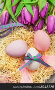 Photo of easter eggs and violet tulips over wooden table