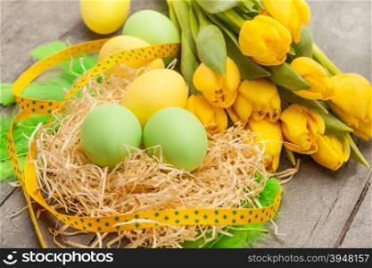 Photo of easter eggs and yellow tulips over wooden table