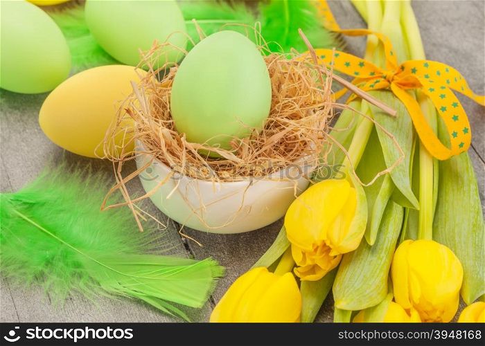 Photo of easter eggs and yellow tulips over wooden table