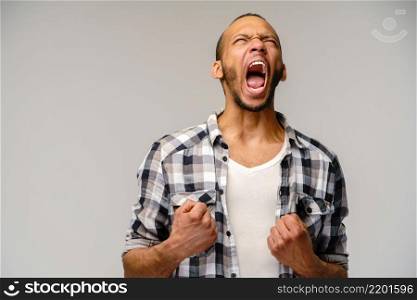 Photo of emotional screaming young african-american man standing over light grey background.. Photo of emotional screaming young african-american man standing over light grey background
