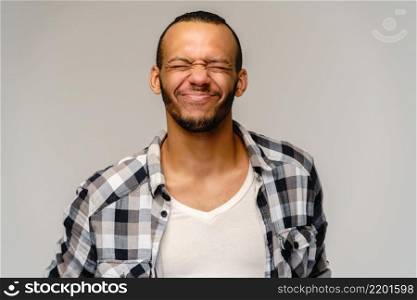 Photo of emotional young african-american man with eyes closed standing over light grey background.. Photo of emotional young african-american man with eyes closed standing over light grey background