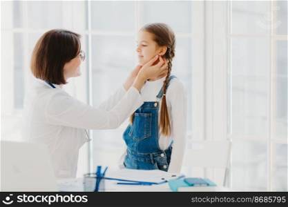 Photo of female pediatrician examines childs throat, being professional skilled pediatrician, consults kid how to prevent tonsillitis, gives good treatment and care. Medical checkup concept.