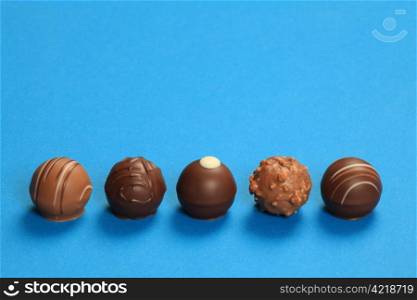 Photo of five chocolate truffles in a row on a blue background.