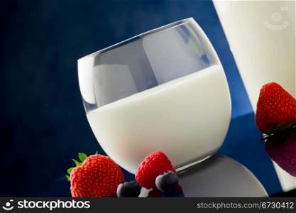 photo of fresh milk on blue glass table with berries around