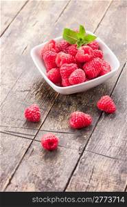 photo of fresh raspberries inside a bowl with mint on wooden table