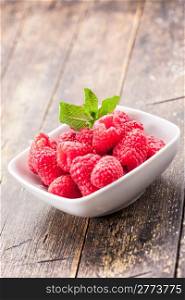 photo of fresh raspberries inside a bowl with mint on wooden table