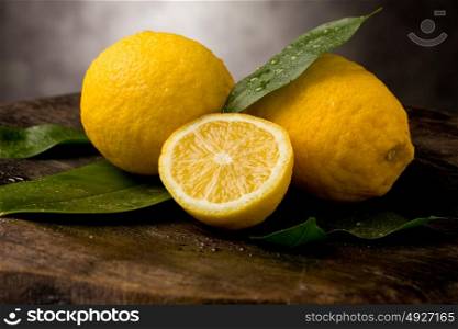 photo of fresh yellow lemons with leaves and water drops on wooden table