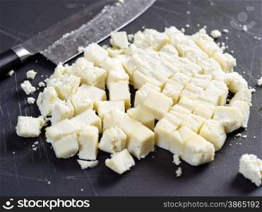 Photo of freshly cut Paneer cheese on a cutting board with knife in the background. Shallow focus across the middle.