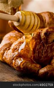photo of golden fresh croissants with honey over on wooden table