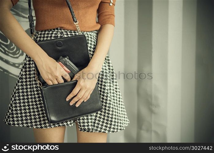Photo of hand of young woman pulling a pistol out of her handbag. Photo of hand of young woman pulling a pistol out of her handbag with free copy space. Self defences concept