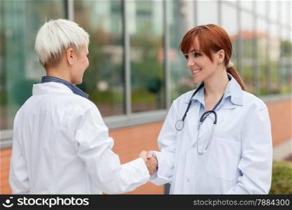 Photo of handshake between two female doctors standing outdoor