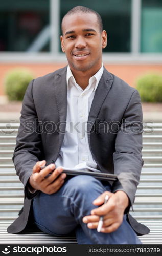Photo of handsome african businessmman sitting on a bench with tablet pc and pen
