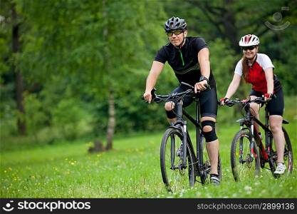 Photo of happy Man and woman exercising with bicycles outdoors, in forest