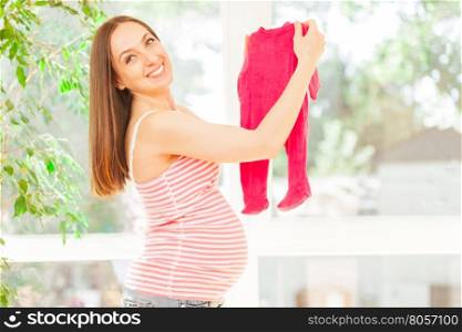 Photo of happy pregnant woman holding baby romper