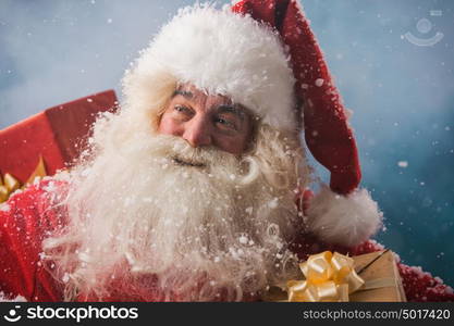 Photo of happy Santa Claus outdoors in snowfall carrying gifts to children