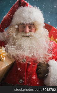 Photo of happy Santa Claus outdoors in snowfall carrying gifts to children