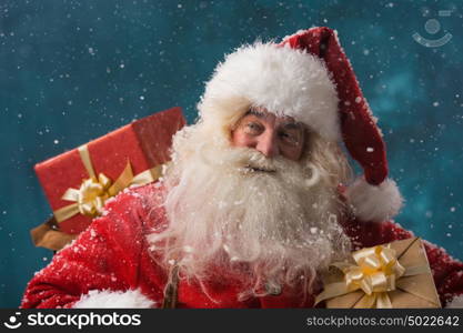 Photo of happy Santa Claus outdoors in snowfall carrying gifts to children