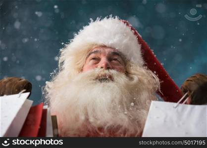 Photo of happy Santa Claus outdoors in snowfall holding shopping bags. Christmas sales and discount concept
