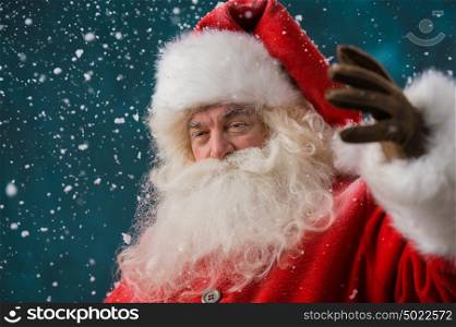 Photo of happy Santa Claus outdoors in snowfall looking at camera and welcoming